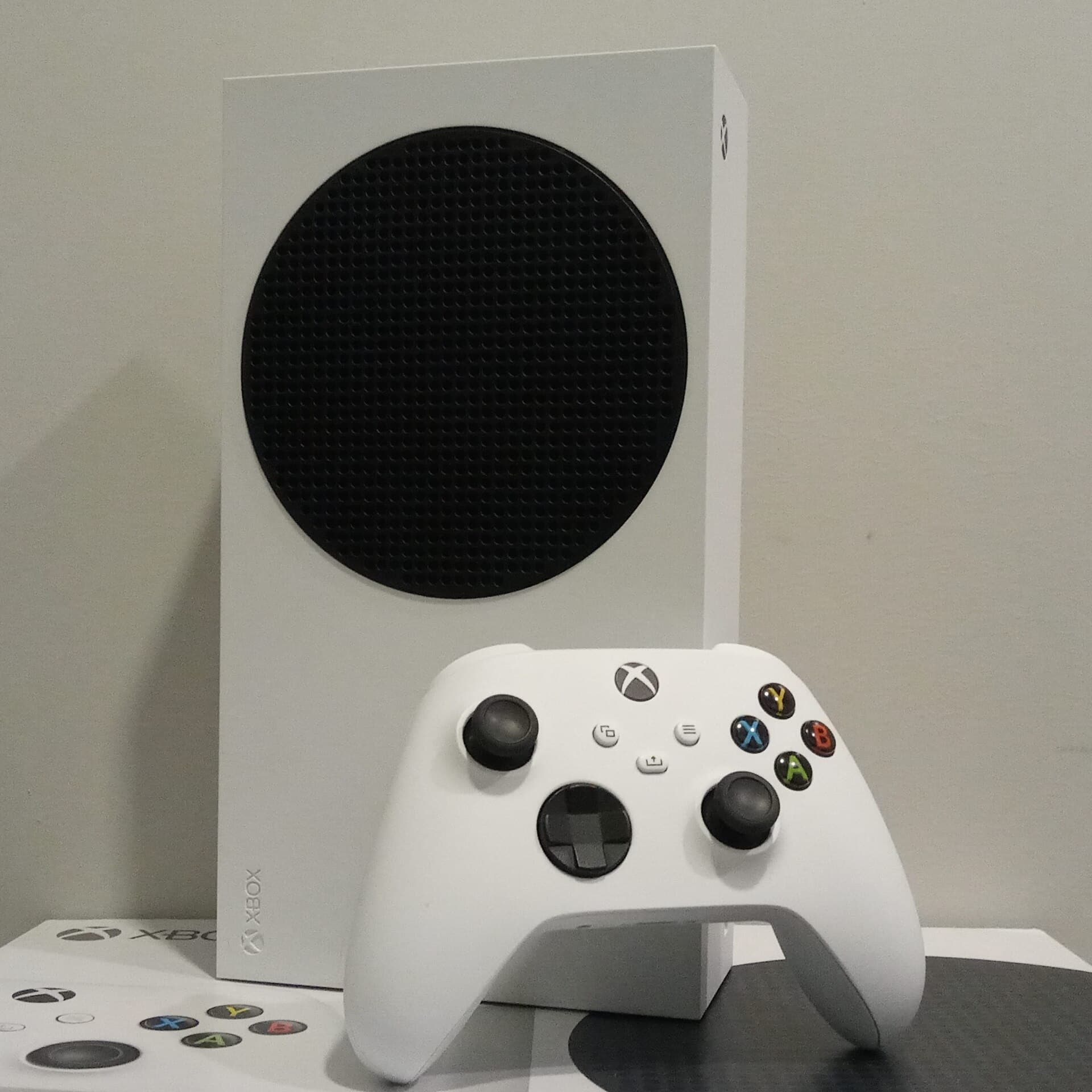 Microsoft Xbox Series S console standing upright, white with a large black circular fan grille, with a white Xbox wireless controller in front