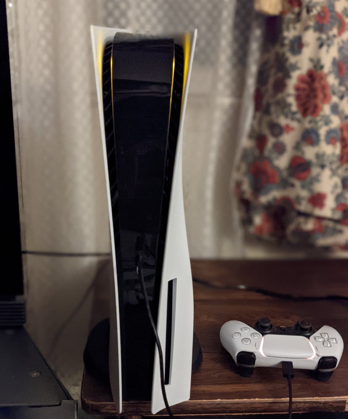 Sony PlayStation 5 console standing vertically on its stand, with a white DualSense wireless controller beside it