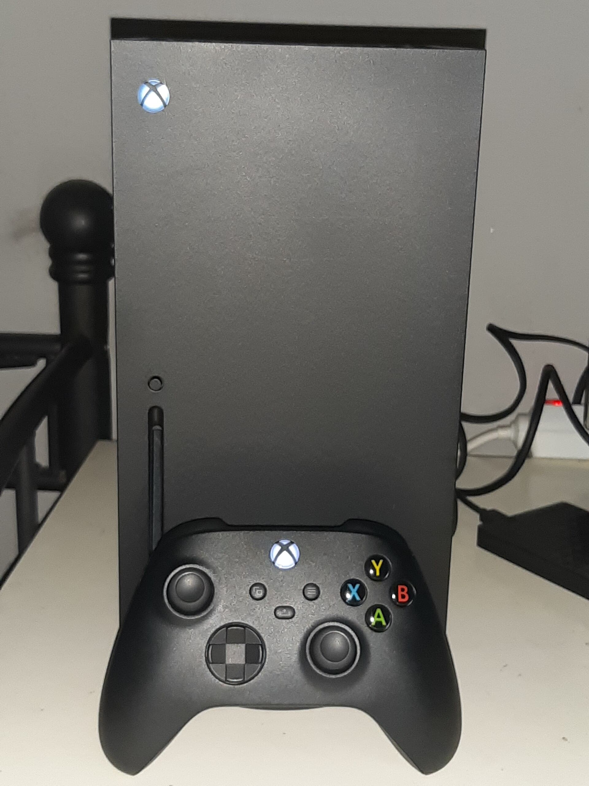 Microsoft Xbox Series X console standing upright with a black Xbox wireless controller in front of it