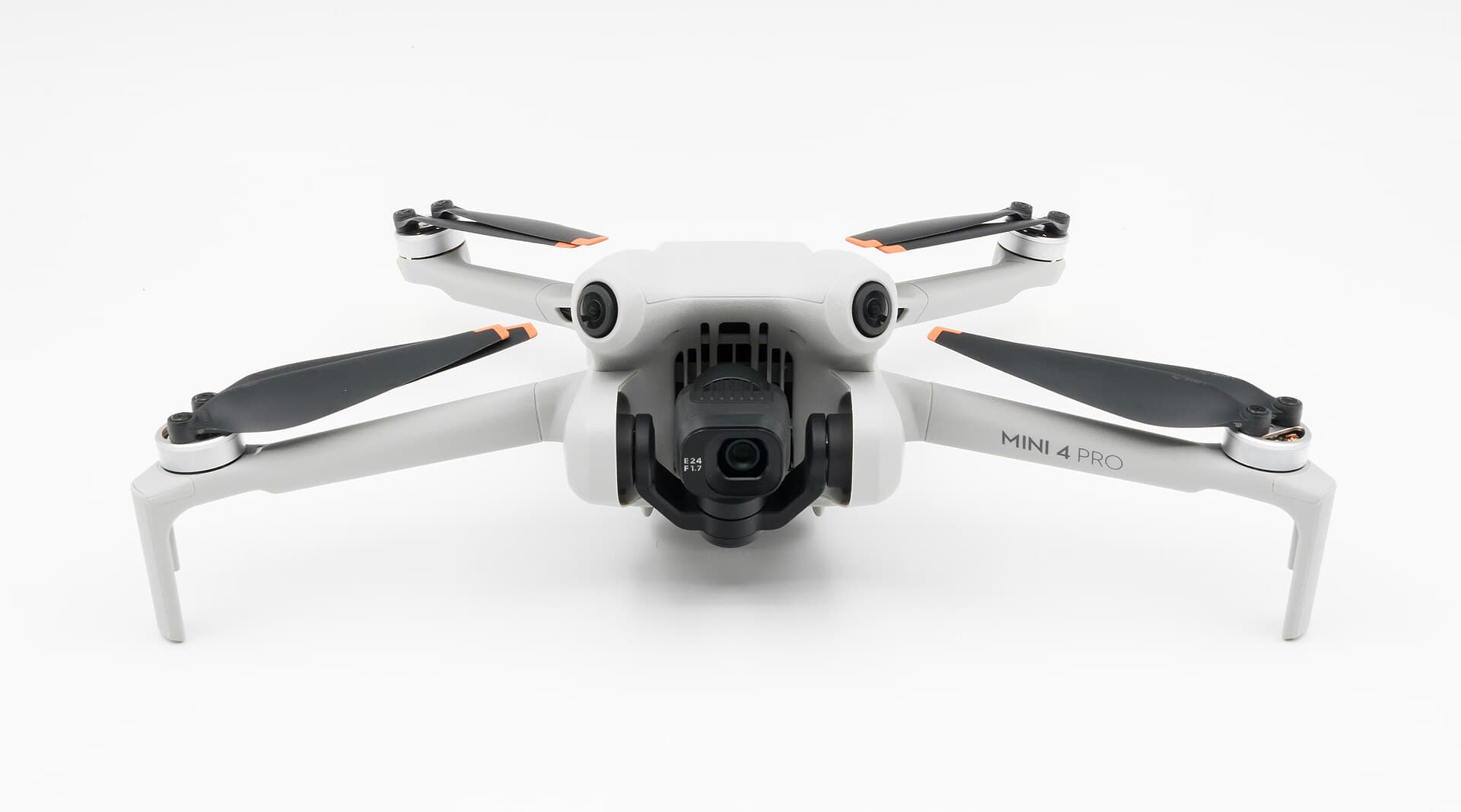 DJI Mini 4 Pro folding camera drone photographed head-on against a white background, arms extended, gimbal camera centred
